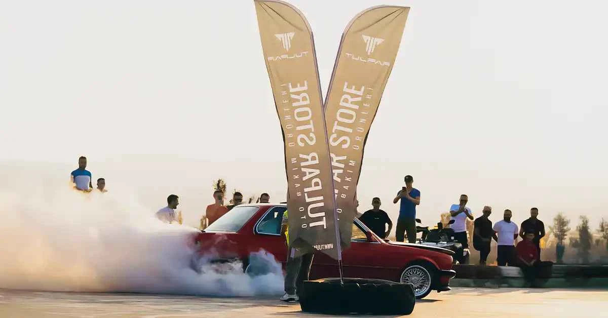 kırmızı renkli bmw e30 aracı tulpar store bayrakları etrafında drift